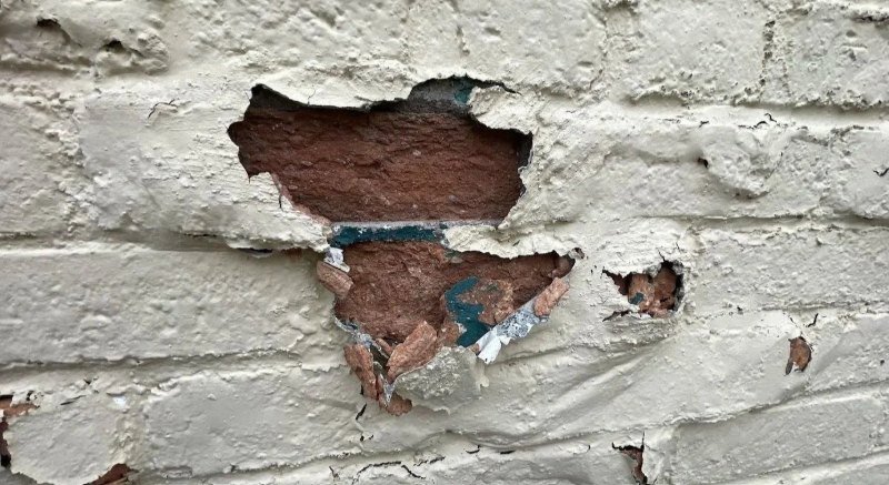 Paint and brick face crumbling off a painted brick wall after moisture was trapped behind the paint