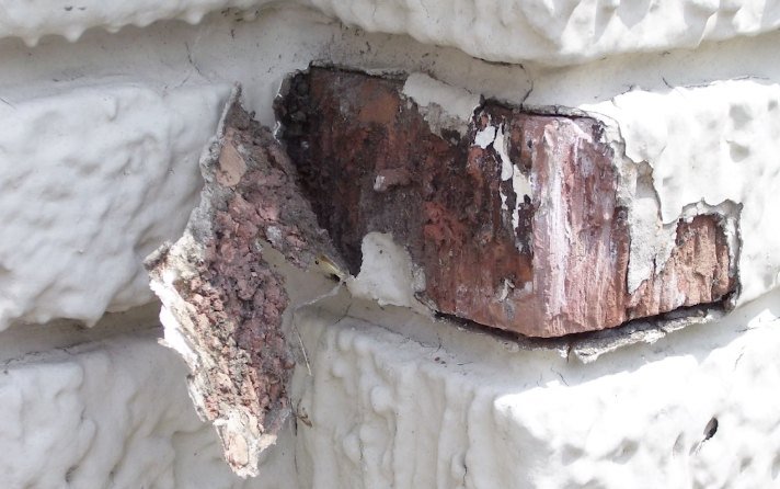 Painted exterior brick spalling, with the face of the brick peeling away along with the paint